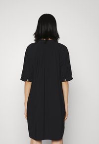 Svart klänning med korta puffärmar och en lös siluett. Har en rynkad halslinning och uppvikt ärmslut med knappar. Slät textur.