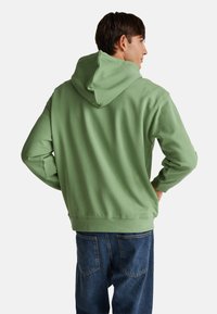 Felpa in cotone verde chiaro con cappuccio regolabile, vestibilità comoda e polsini a costine, abbinata a jeans in denim blu.