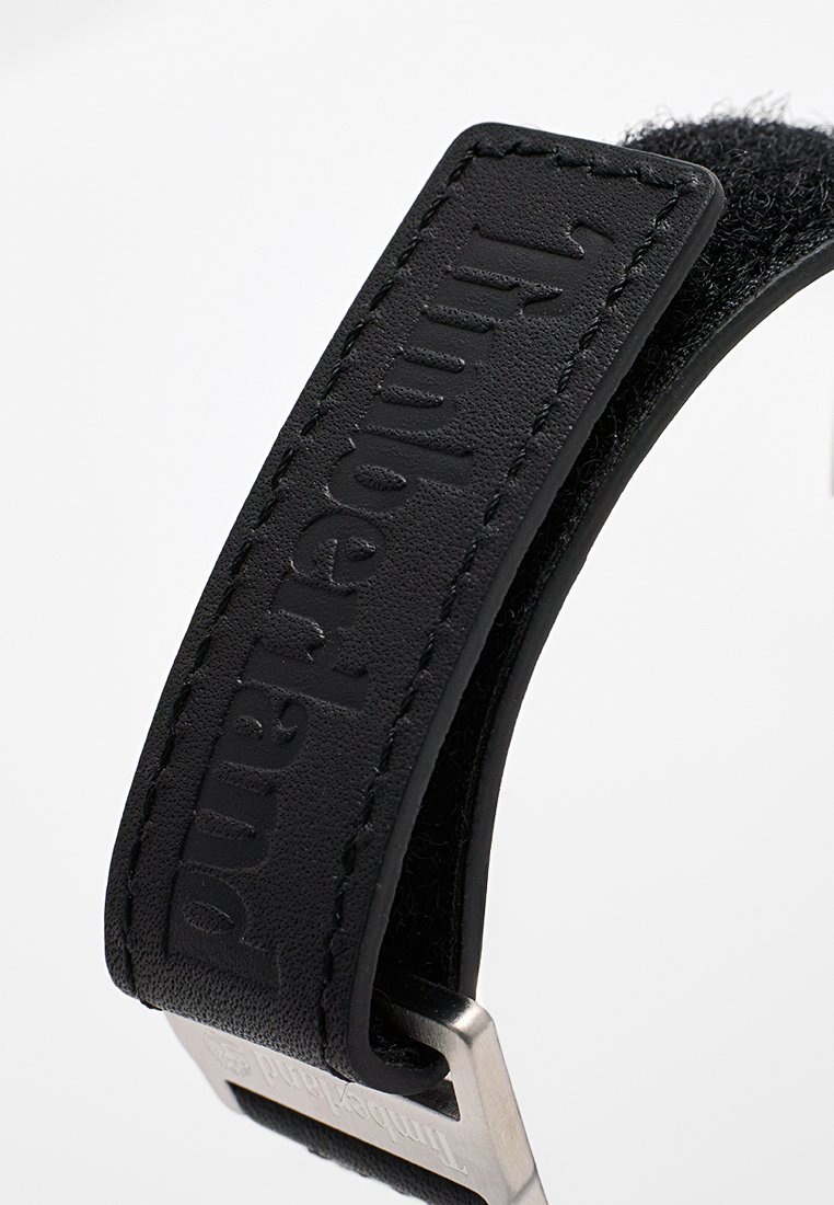 Correa de cuero negro con marca en relieve, bordes cosidos y una hebilla de metal con texto grabado. Superficie texturizada para un mejor agarre.