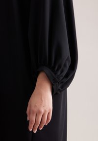 Czarny, lejący się strój z marszczonym rękawem zakończonym mankietem na guziki, gładka tekstura i prosty, elegancki design.