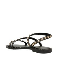 Schwarze Sandalen mit einem Riemendesign und goldenen Nieten, flachen Sohlen und einer glatten Textur. Die Riemen sind im Überkreuzmuster angeordnet.