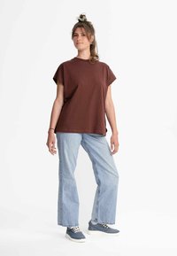 Braunes, kurzes T-Shirt mit kurzen Ärmeln, kombiniert mit hellblauen, weit geschnittenen Jeans und blauen Turnschuhen. Minimalistisches Design mit schlichten Linien.