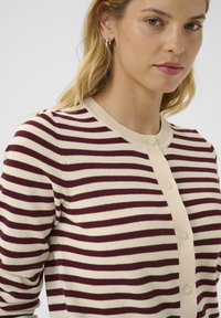 Knitted cardigan with maroon and cream horizontal stripes. Features a round neckline and front button closure with lightweight texture.