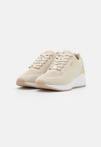 Béžové sportovní boty s síťovinou, šněrovacím designem, zlatými akcenty a texturovanou podrážkou. Mají lehkou konstrukci.