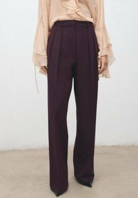 Pantalones de tiro alto en burdeos oscuro con pliegues, piernas rectas y una textura suave, combinados con una blusa ligera con volantes.
