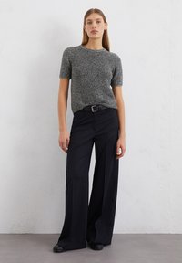 Grijze en zwarte gemêleerde gebreide top met korte mouwen, gecombineerd met hoog-waist navy palazzo-broeken en een zwarte riem. Zwarte schoenen maken de outfit compleet.