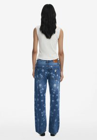 Wijde blauwe denim jeans met bloemendruk, een vervaagde uitstraling en een bruine merketiket op de tailleband. Heeft twee achterzakken.