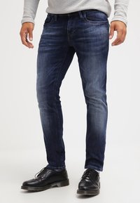 Mörkblå denimjeans, slim fit, med lätt blekning på låren. Bärs med svarta dressade skor. Standard femficksdesign.
