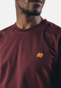 Bordeauxfarbene Baumwoll-T-Shirt mit einem kleinen gelben gestickten Elefantenlogo auf der linken Brustseite. Weicher Stoff mit klassischer Passform.
