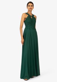 Groene avondjurk met ingewikkelde bloemenkantdetails op het lijfje, hoge halslijn en een vloeiende rok. Elegante textuur.