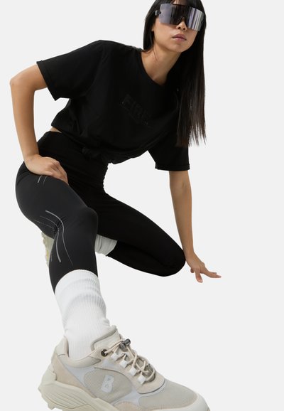 Czarny top crop z detalem "FIRE", czarne legginsy z białymi akcentami oraz beżowe sneakersy sportowe z teksturowanym wykończeniem.