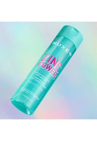 Bottiglia di plastica turchese del tonico Nuxe Zinc Power con tappo a scatto. Presenta un testo rosa intenso e dettagli in argento. Capacità di 200 ml.