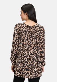 Chemisier à manches longues imprimé animal ; couleurs beige et noir ; tissu doux avec des détails plissés et une petite fermeture à bouton à l'arrière.