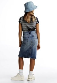 Gonna di denim con tasche posteriori, vita aderente e forma ad A. Abbinata a una camicia a righe bianche e nere e a un cappello a secchiello azzurro chiaro.