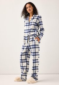 Rutig flanellpyjamas-set i blått och vitt, bestående av en långärmad skjorta med knappar och byxor med resår i midjan och fickor, i kombination med beige tofflor.