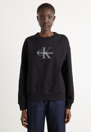 Sort crewneck sweatshirt lavet af bomuldsblanding, med et centreret hvidt og gråt "Calvin Klein" logo samt ribbede manchetter og bund.