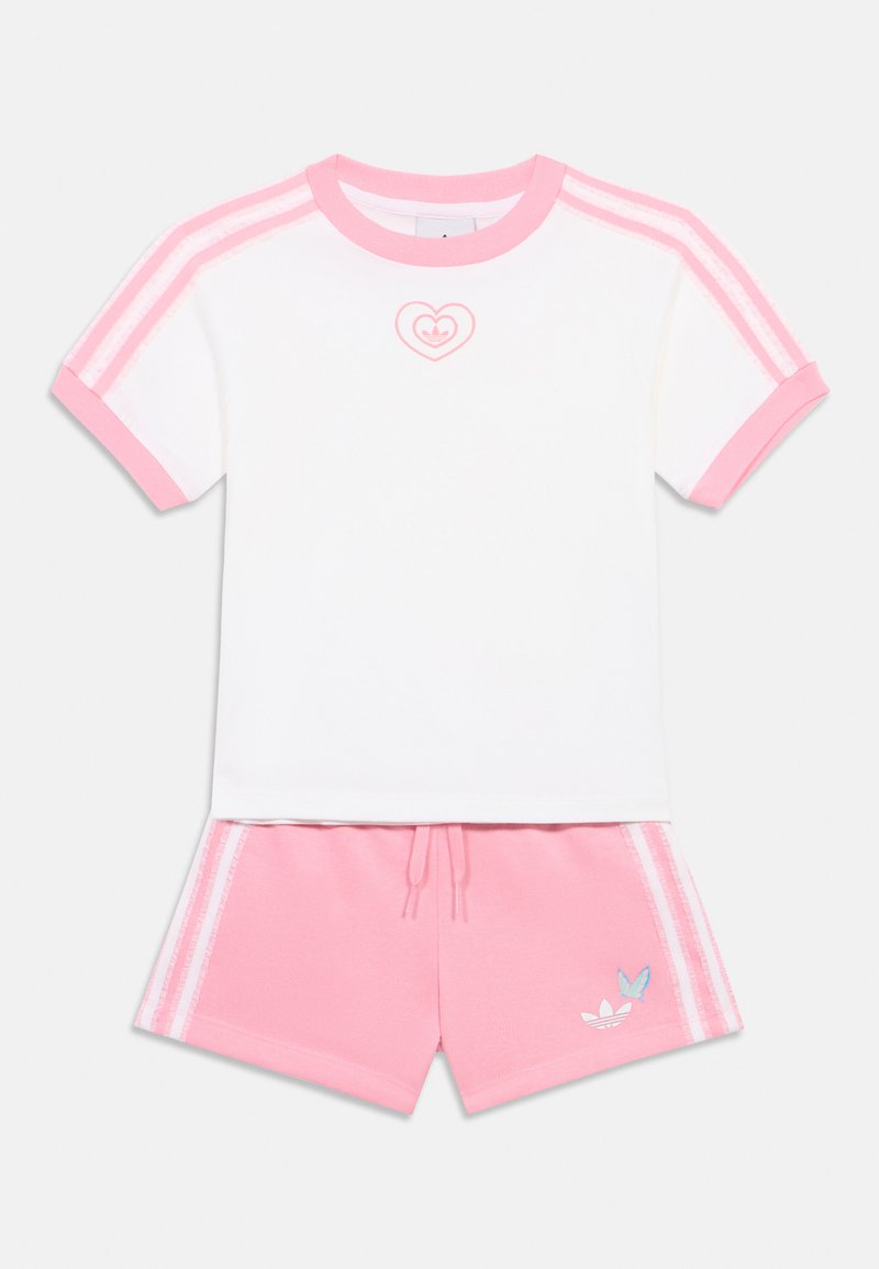 Rövid ujjú fehér felső rózsaszín részletekkel és szív logóval, rózsaszín rövidnadrággal, fehér csíkokkal és kék logóval. Pamut keverék anyag.