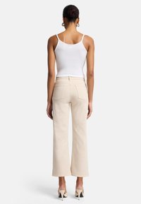 Jeans larges beige à taille haute, avec poches arrière visibles et détails de couture subtils. Associés à un débardeur blanc et des chaussures à talons.