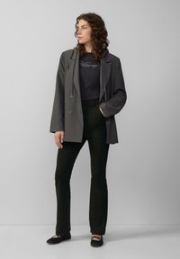 Grijze pinstriped blazer met een losse fit, gecombineerd met een donkere top en zwarte broek. De schoenen zijn zwarte ballerina's met gekruiste banden.
