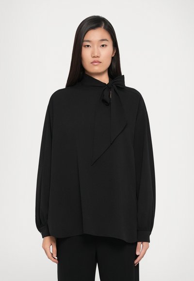 Mustapaita, jossa on solmu kauluksessa, pitkät puffhihaiset hihat ja väljä muotoilu. Valmistettu sileästä kankaasta, minimalistic design, ei kuvioita.