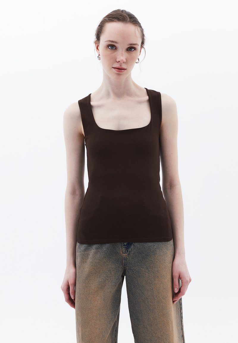Top senza maniche marrone con scollatura quadrata, realizzato in tessuto liscio. Abbinato a pantaloni in denim leggeri e larghi.