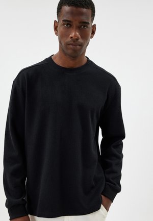 Schwarzes langärmliges Thermoshirt mit gerippter Textur, runder Ausschnitt und lockerer Passform. Einfaches Design ohne sichtbare Muster.