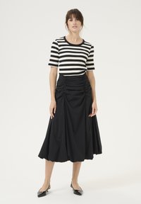 Mustmust keha, mis on kombineeritud musta ja valge triibulise lühikese varrukaga topiga. Seelikul on voolav disain ja tekstuuriga kangas. Seljas mustad lamedad kingad.