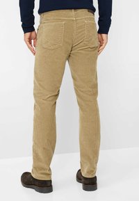 Pantaloni in corduroy color beige con righe verticali, cinque tasche e vestibilità regolare. Caratterizzati da una vita con passanti per cintura e stivali marroni.
