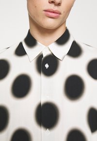 Hemden mit Knopfleiste aus leichtem Stoff mit weißem Grund, großen schwarzen Kreisen und sanft grauen Rändern. Klassischer Kragen mit Knopfverschluss.