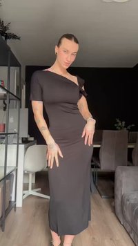 Vestido preto justo com design de um ombro, textura suave e comprimento até a metade da panturrilha. O tecido cai suavemente e tem um brilho sutil.