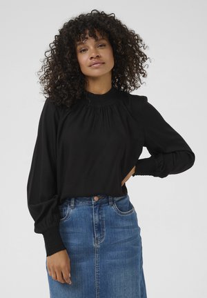 Zwarte blouse met lange mouwen, hoge halslijn, smockdetails en aansluitende manchetten, gecombineerd met een blauwe denimrok.