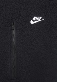 Svart fleecepулlover med halv dragkedja och texturerad yta; har en vit Nike-logga på övre vänstra bröstområdet.