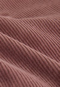 Tela de algodón acanalada de color rosa polvo suave, con estrías paralelas y pliegues suaves que crean una superficie texturizada y ondulada.