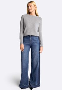 Pulover tricotat de culoare gri deschis cu guler rotund, asociat cu blugi din denim albastru cu picioare largi, având talie înaltă și margini desfăcute.
