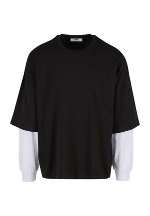 Camiseta negra de manga corta con mangas largas blancas superpuestas, hecha de un tejido suave, con un escote redondeado y un corte holgado.