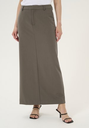 Jupe maxi en tissu marron foncé avec une texture lisse et un détail de fente à l'avant. Portée avec des sandales à talons hauts noires à lanières.