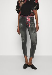 Černý květinový top s volnými rukávy, spárovaný s odřenými šedými džíny. Džíny mají třepený lem, abstraktní skvrny a vzorovaný pásek. Černé baleríny.