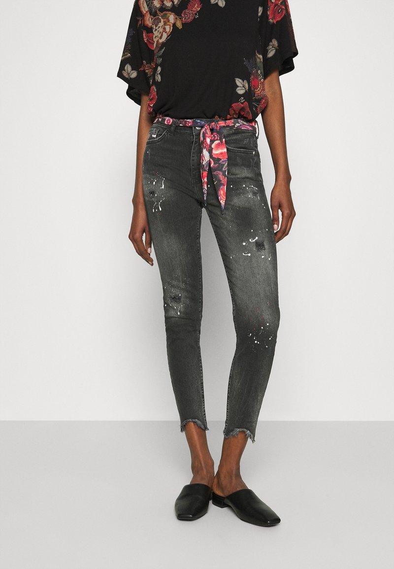 Černý květinový top s volnými rukávy, spárovaný s odřenými šedými džíny. Džíny mají třepený lem, abstraktní skvrny a vzorovaný pásek. Černé baleríny.