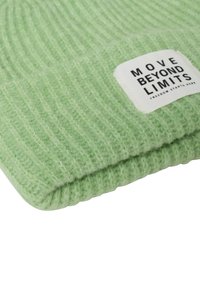 Miętowa zielona dziana czapka z prążkowaną fakturą. Posiada biały tag z napisem "MOVE BEYOND LIMITS" w czarnym tekście. Miękki, przytulny materiał.