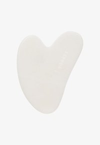 Herramienta de masaje facial gua sha en forma de corazón blanco con la marca "Korres" sobre un fondo liso.