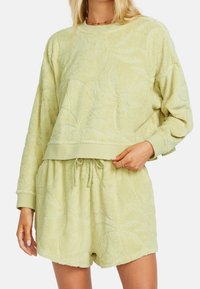 Světlý zelený froté lounge set s embosovanými vzory listů; obsahuje dlouhý rukáv a kraťasy na stažení. Měkká textura, pohodlný střih.