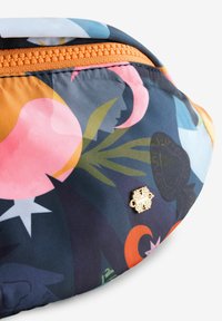 Värikäs kangaspussi, jossa abstrakteja kukka- ja geometrisia kuvioita. Oranssi vetoketjusuljin ja koristeelliset kullanväriset metalliosat.