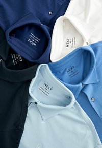Fünf Poloshirts in verschiedenen Farben: marineblau, dunkelgrün, hellblau, weiß und blassblau. Jedes Shirt hat einen klassischen Kragen und Markenetiketten.