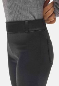 Leggings negros de cintura alta con una textura suave y elástica, que cuentan con un bolsillo lateral y una cinturilla gruesa y elástica.