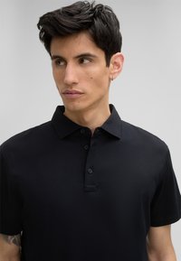 Czarna koszulka polo wykonana z gładkiego materiału, z kołnierzykiem i zapięciem na trzy guziki. Krótkie rękawy i minimalistyczny design.