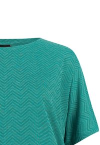 Chemise à manches courtes couleur sarcelle avec un motif en zigzag subtil et un col rond, montrée de la partie supérieure de la poitrine à l'épaule.