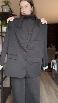 Giacca nera con rever a punta, chiusura a un bottone, due tasche frontali e polsini bianchi a contrasto. Il materiale appare liscio.