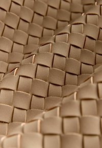 Szőtt bőr anyag világos barna színben, strukturált felülettel, négyzet és téglalap formákból álló rácsmintázattal.