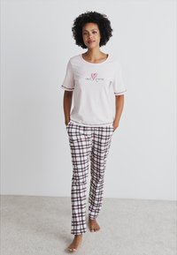 T-shirt de algodão rosa claro com gráfico "tempo para mim"; combinado com calças de pijama xadrez em branco, rosa e preto. Textura suave com corte relaxado.