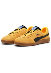 Suède gele sneakers met een zwarte zijkantstreep, ronde neus en rubberen zool. Voorzien van een zwarte tong en blauwe branding op de bovenkant.